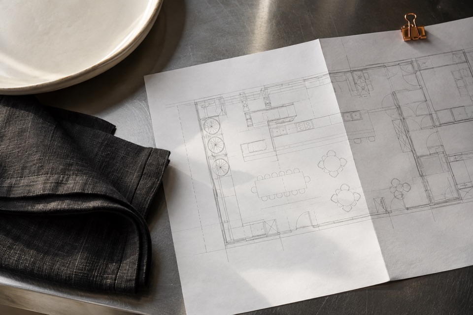 Illustration of kitchen plans beside a plate and linen on a worktop